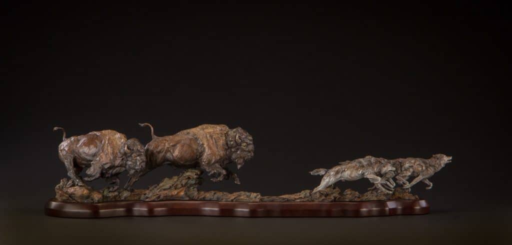A bronze wildlife sculpture of buffalo chasing wolves.