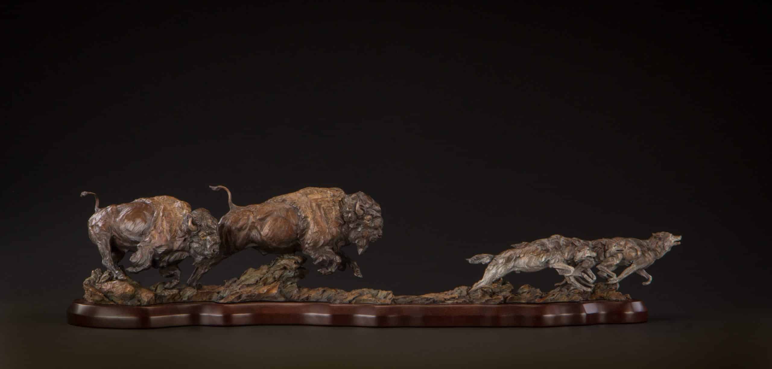 A bronze wildlife sculpture of buffalo chasing wolves.