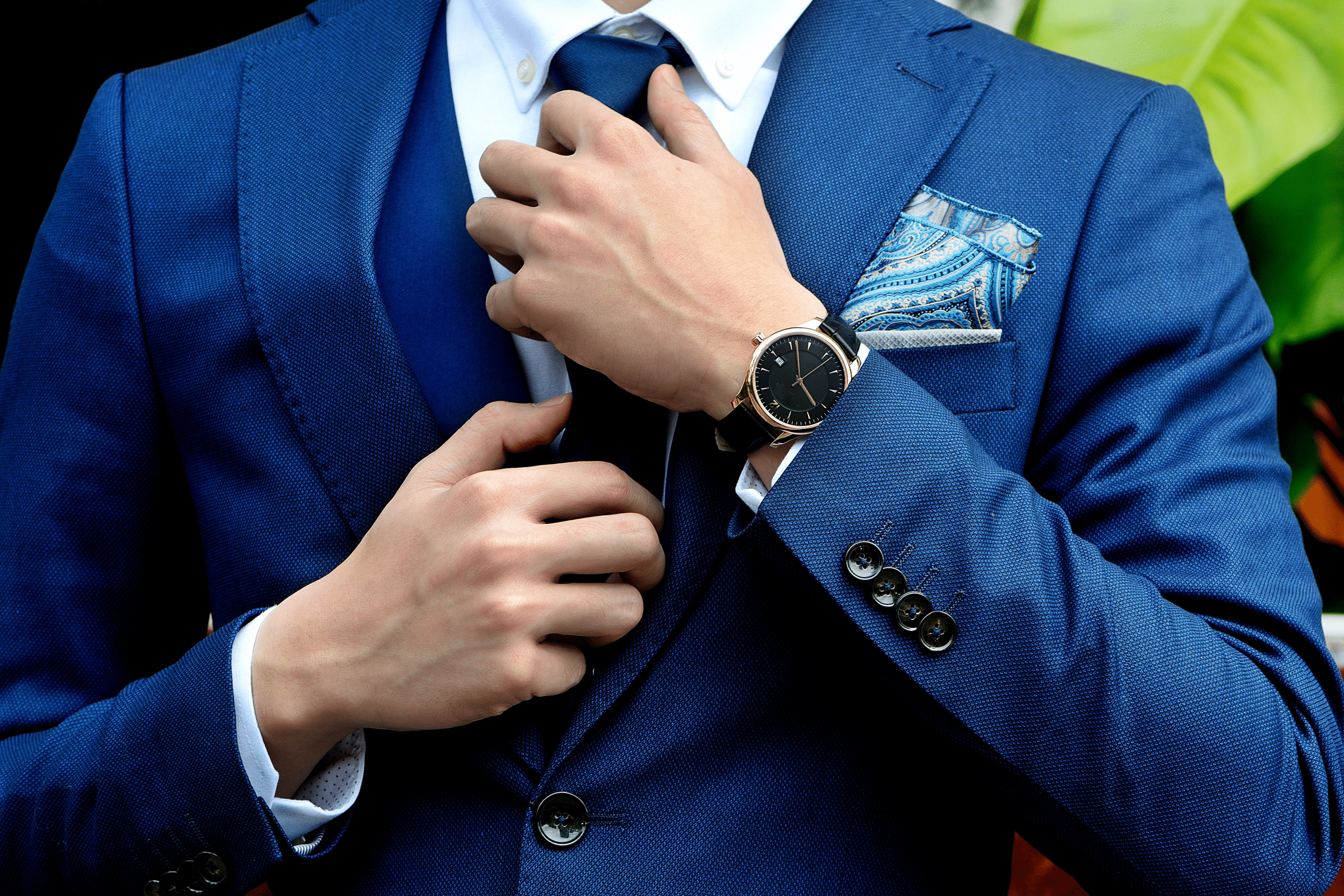 A man in a blue, three-piece suit adjusts his tie.